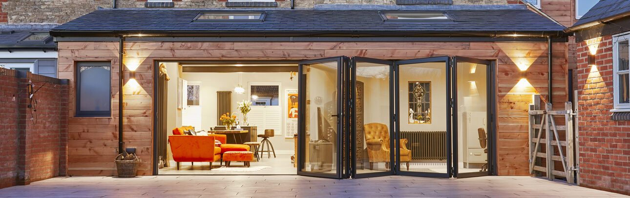 Cedar-clad rear extension with bifold doors at dusk